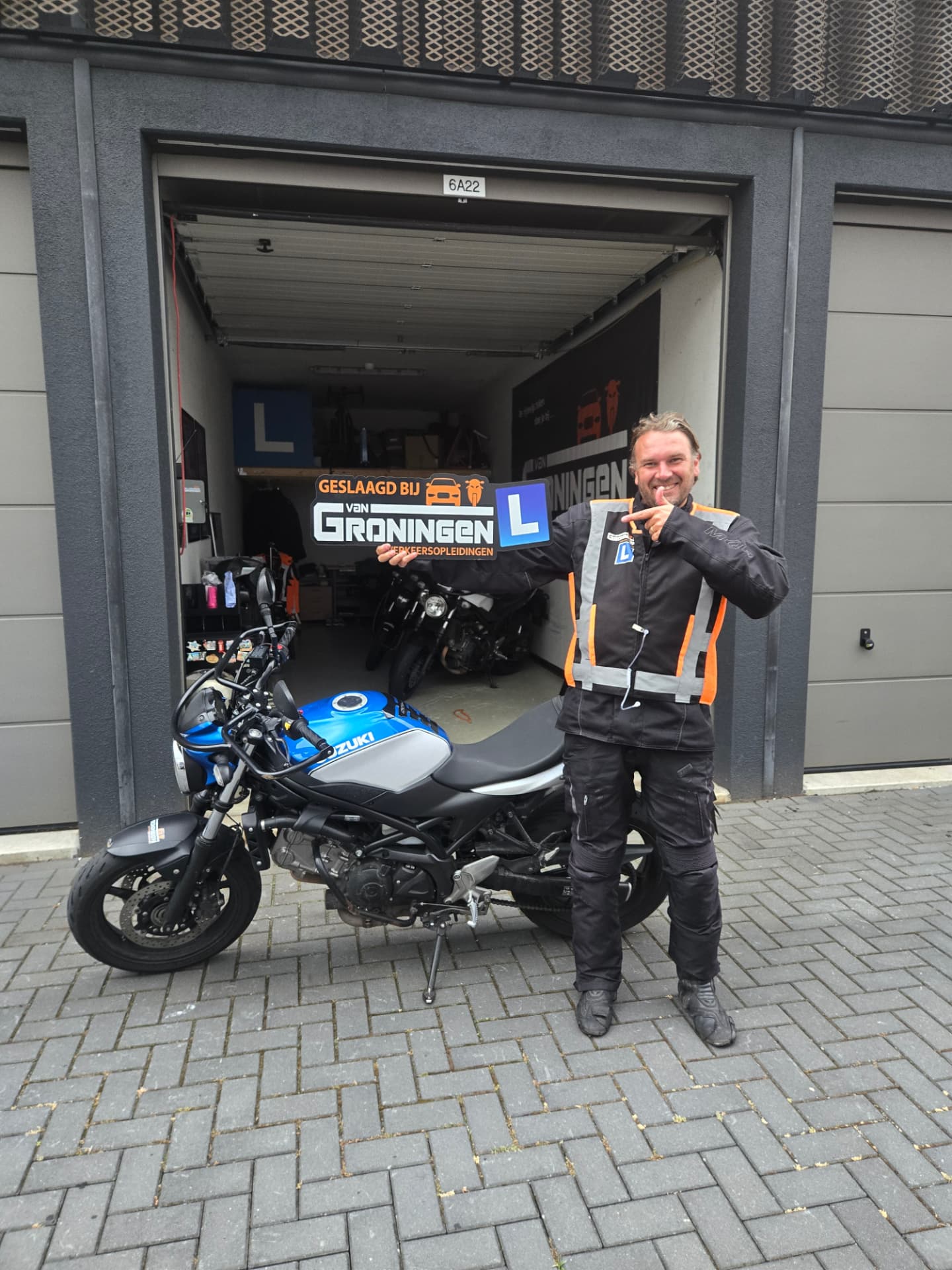Geslaagde motorleerling in motorkleding bij de lesmotor